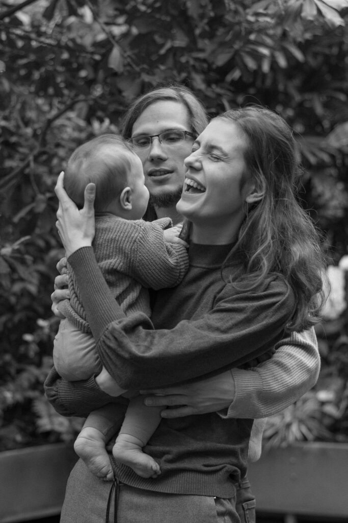 Schwarz-weißes Familienfoto mit einer Frau, einem Mann und einem Kleinkind, die sich umarmen und zusammen lachen.