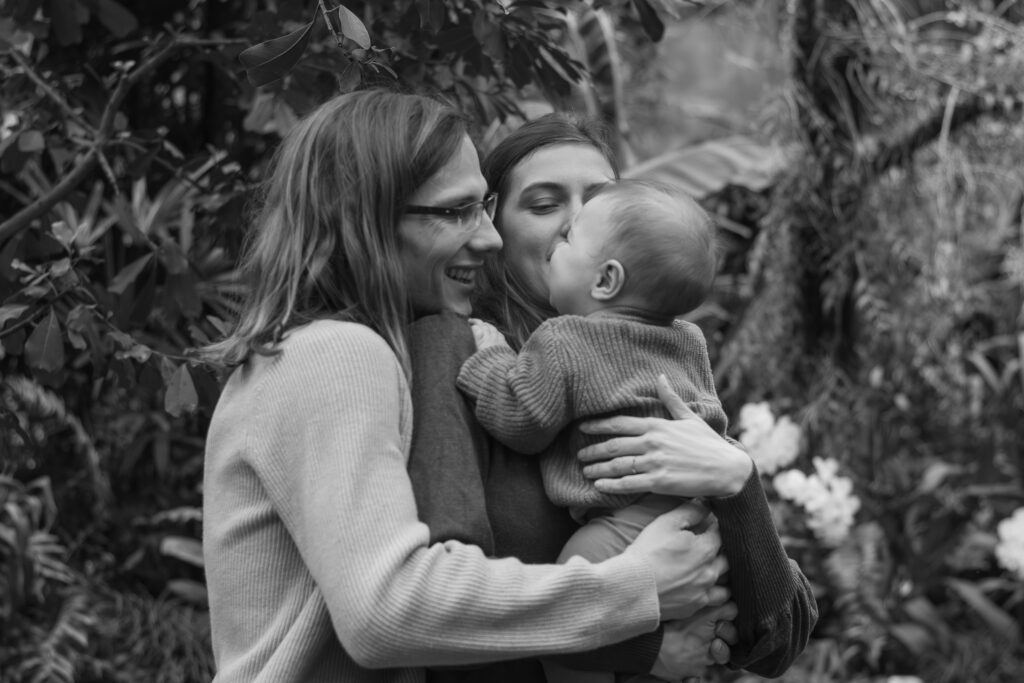 Schwarz-Weiß-Foto aus einem Familienshooting mit einer Familie mit einer Frau, einem Mann und einem Kleinkind, die sich umarmen und lachen.